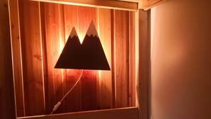 Un lit surmonté d’un luminaire en forme de montagne, un mur recouvert de lambris en bois et un couvre-lit blanc à rayures rouges.
