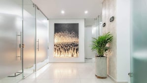 Una moderna zona de recepción con un panel de vidrio, un cuadro abstracto de gran tamaño y una planta en maceta.
