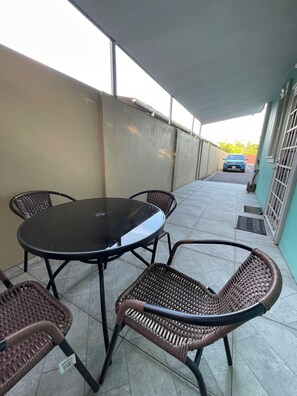 Ein überdachter Patio-Bereich mit einem runden Tisch und vier Korbstühlen.