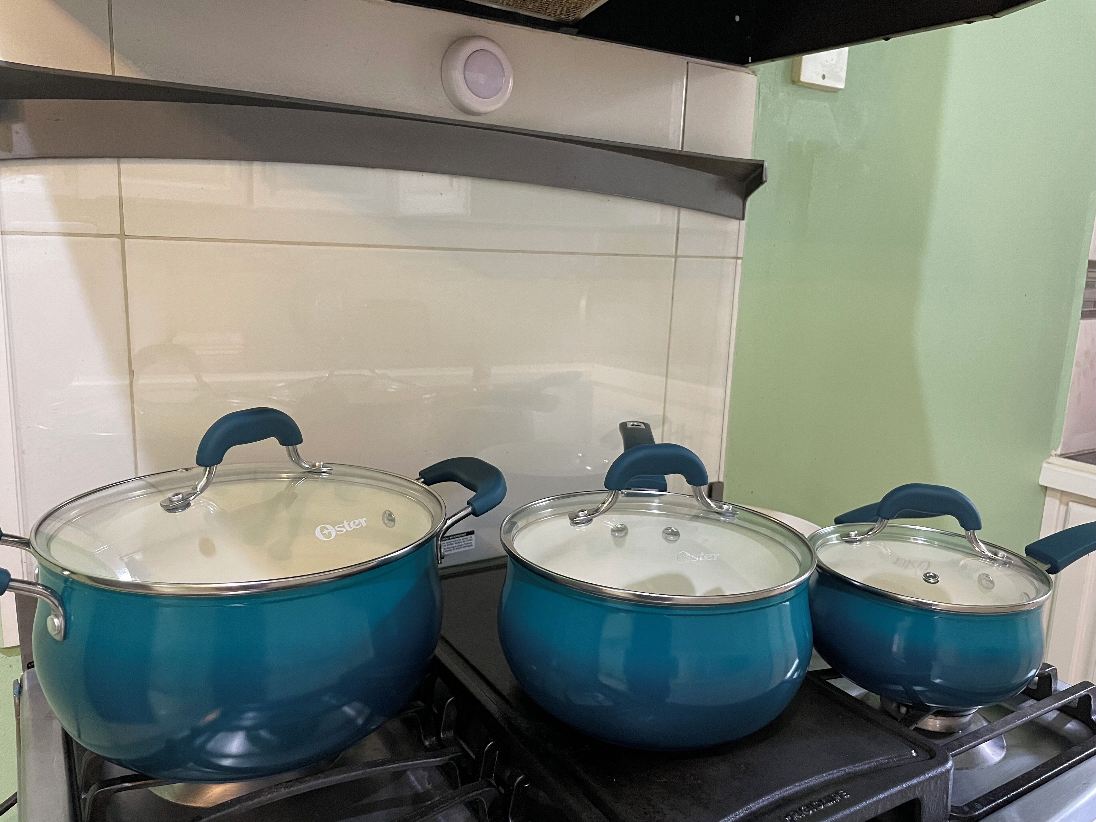 Tres ollas azules sobre una estufa con un salpicadero de azulejos y una pared verde.