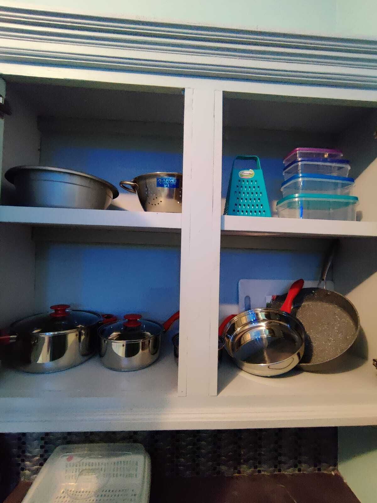 A kitchen shelf with various kitchenware including pots, pans, and containers.