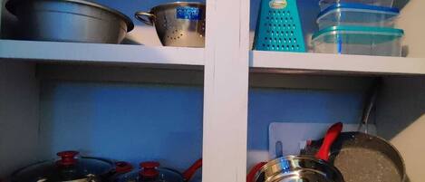 A kitchen shelf with various kitchenware including pots, pans, and containers.