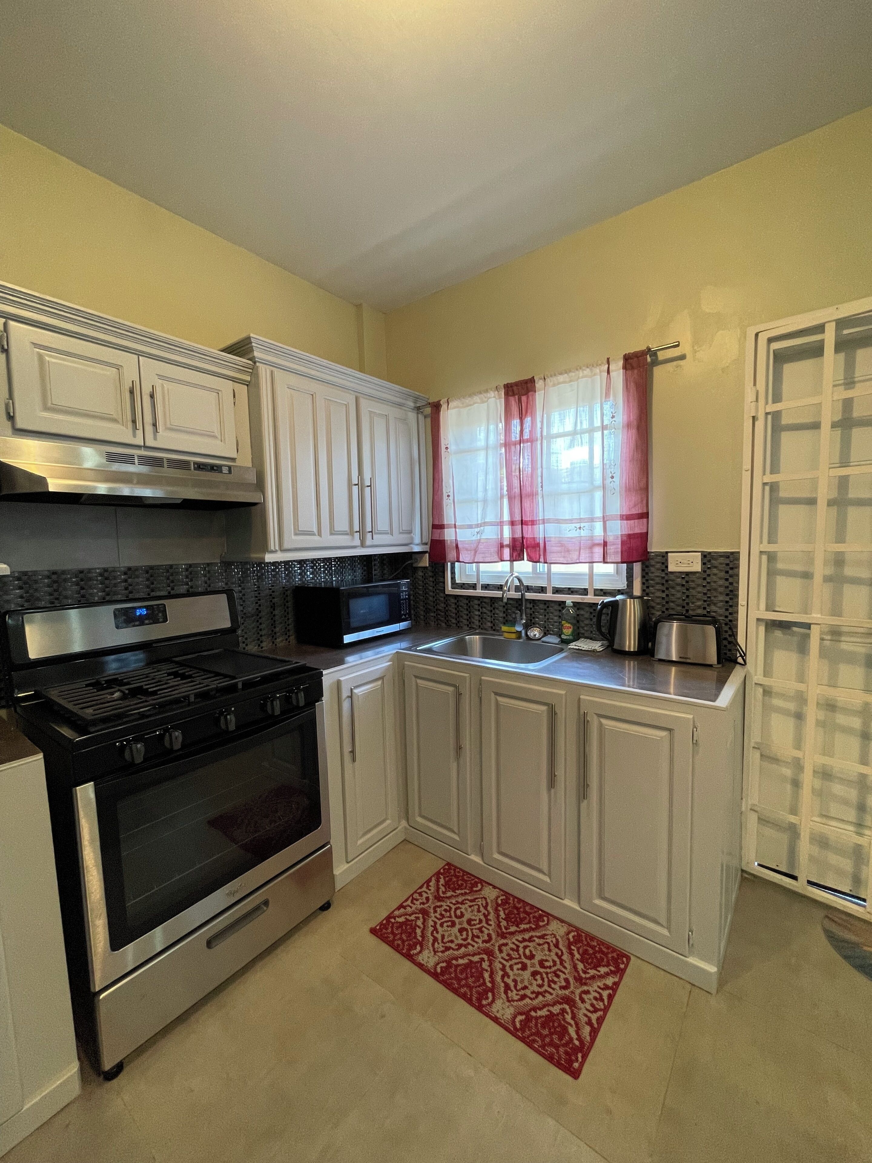 Una cocina con armarios blancos, estufa de acero inoxidable, microondas y lavaplatos.