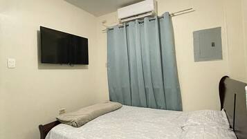 Ein Schlafzimmer mit einem Bett, einem an der Wand montierten Flachbildfernseher, einer Klimaanlage und einer Steckdose.