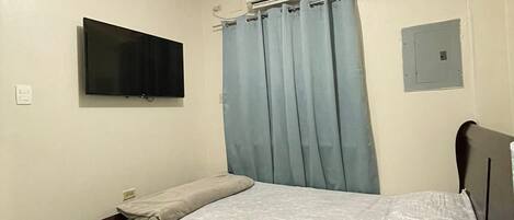 Un dormitorio con cama, televisor de pantalla plana montado en la pared, equipo de aire acondicionado y toma de corriente.