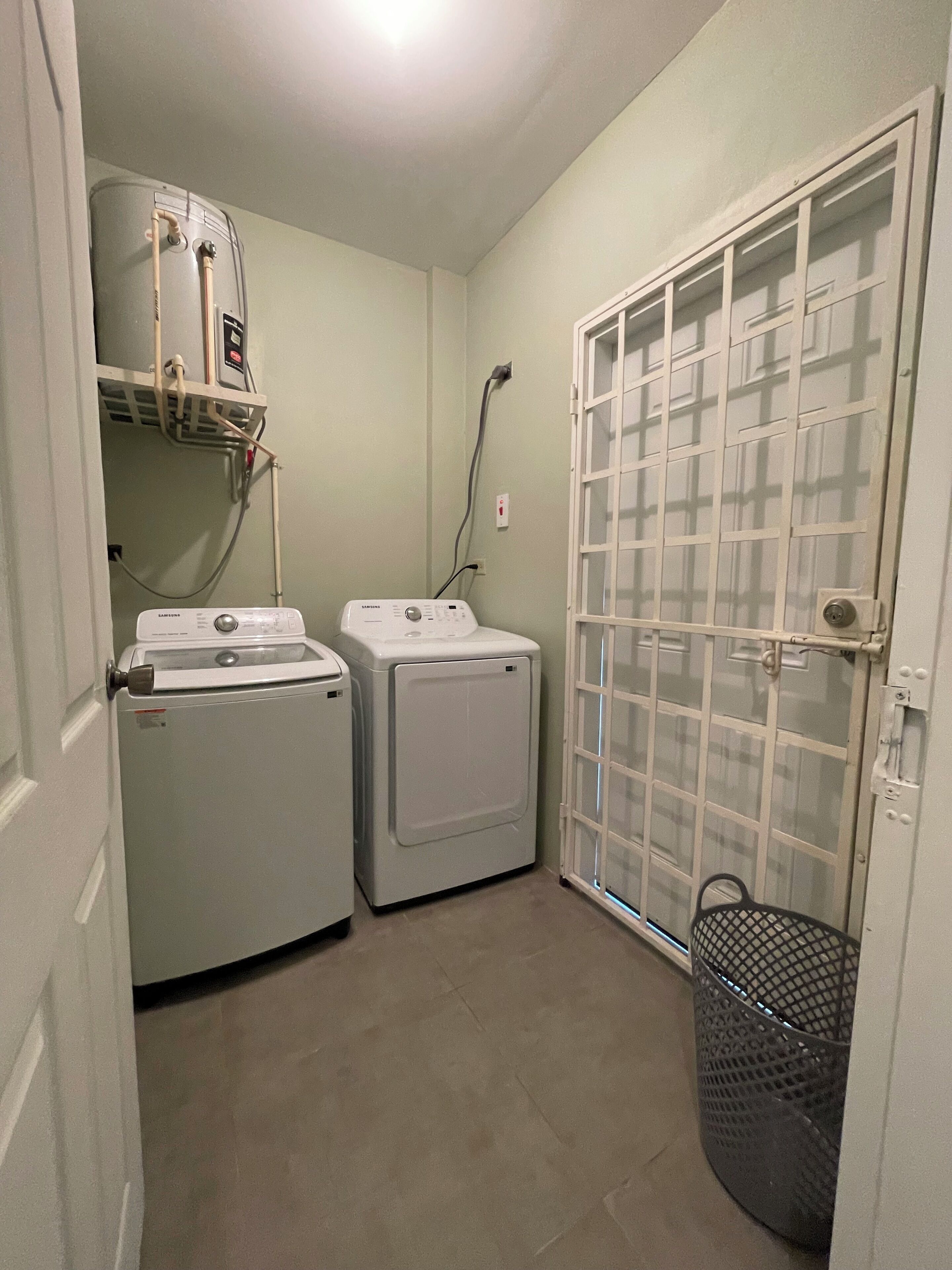 A laundry room with two washing machines, a water heater, and a utility closet with a metal basket.