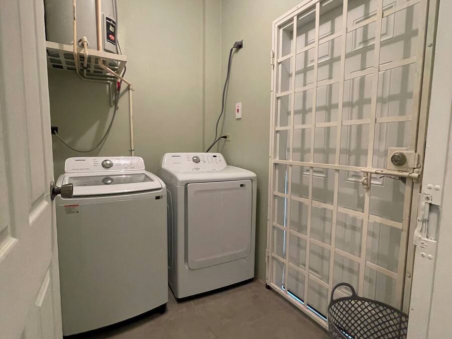 Un cuarto de lavandería con dos lavadoras, un calentador de agua y un armario de servicios con una cesta de metal.