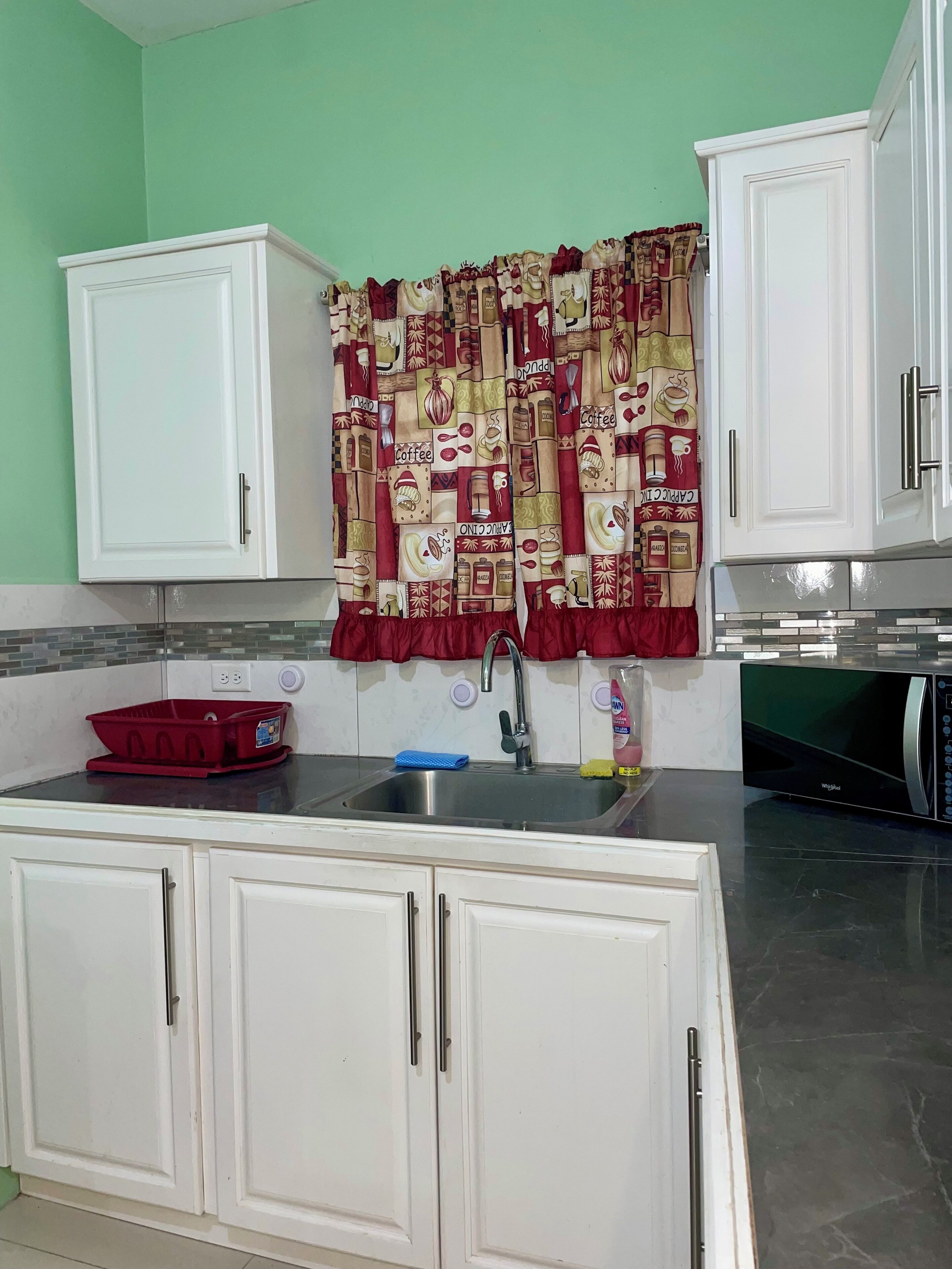 Una cocina con armarios blancos, un lavamanos de acero inoxidable y un microondas.