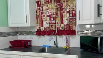 Una cocina con armarios blancos, un lavamanos de acero inoxidable y un microondas.