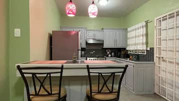 A kitchen with a central island, two bar stools, a refrigerator, and a stove.