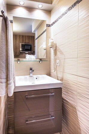 Une salle de bain moderne avec un lavabo surmonté d’une plaque de verre, un miroir, un téléphone et des meubles en bois.