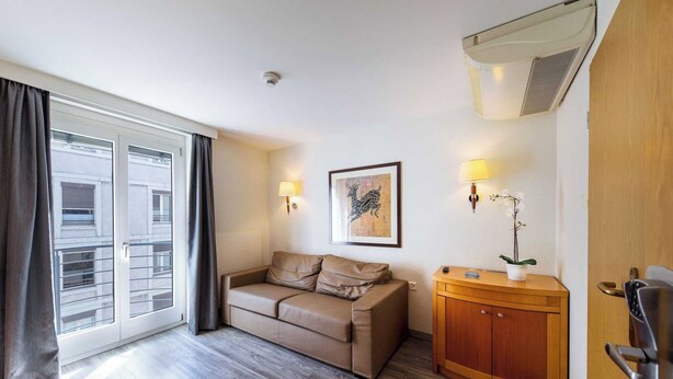 Une chambre d’hôtel avec un canapé, une armoire en bois, une lampe fixée au mur et un tableau encadré.