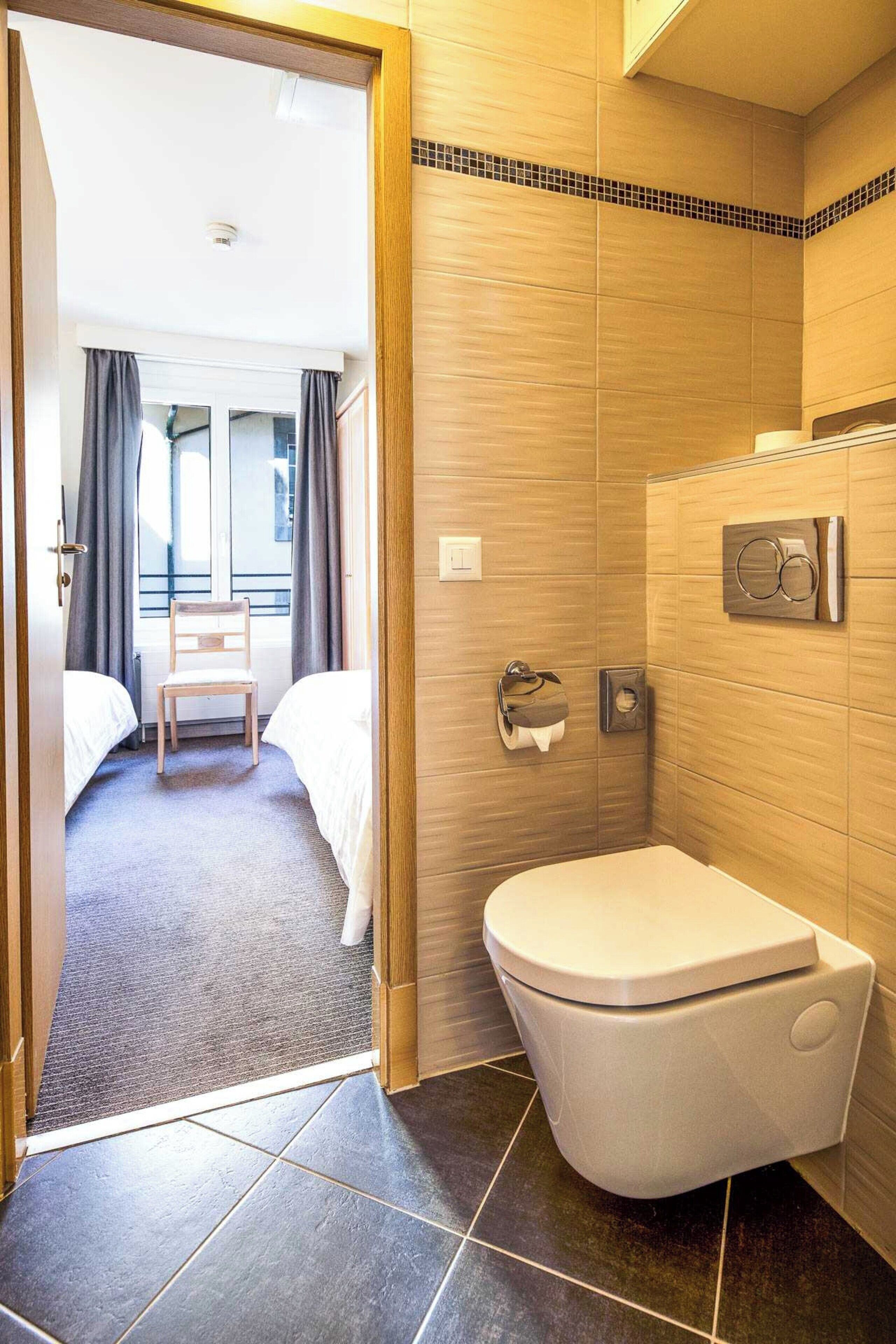A hotel room with a bathroom, a bed, a chair, and a toilet.