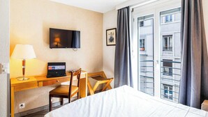 Une chambre d’hôtel avec un lit, un bureau avec un ordinateur portable, une télévision et une fenêtre avec des rideaux.
