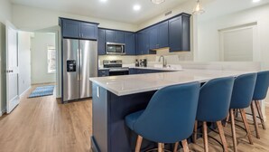 Una cocina moderna con armarios azul oscuro, electrodomésticos de acero inoxidable y una isla central con taburetes de bar.