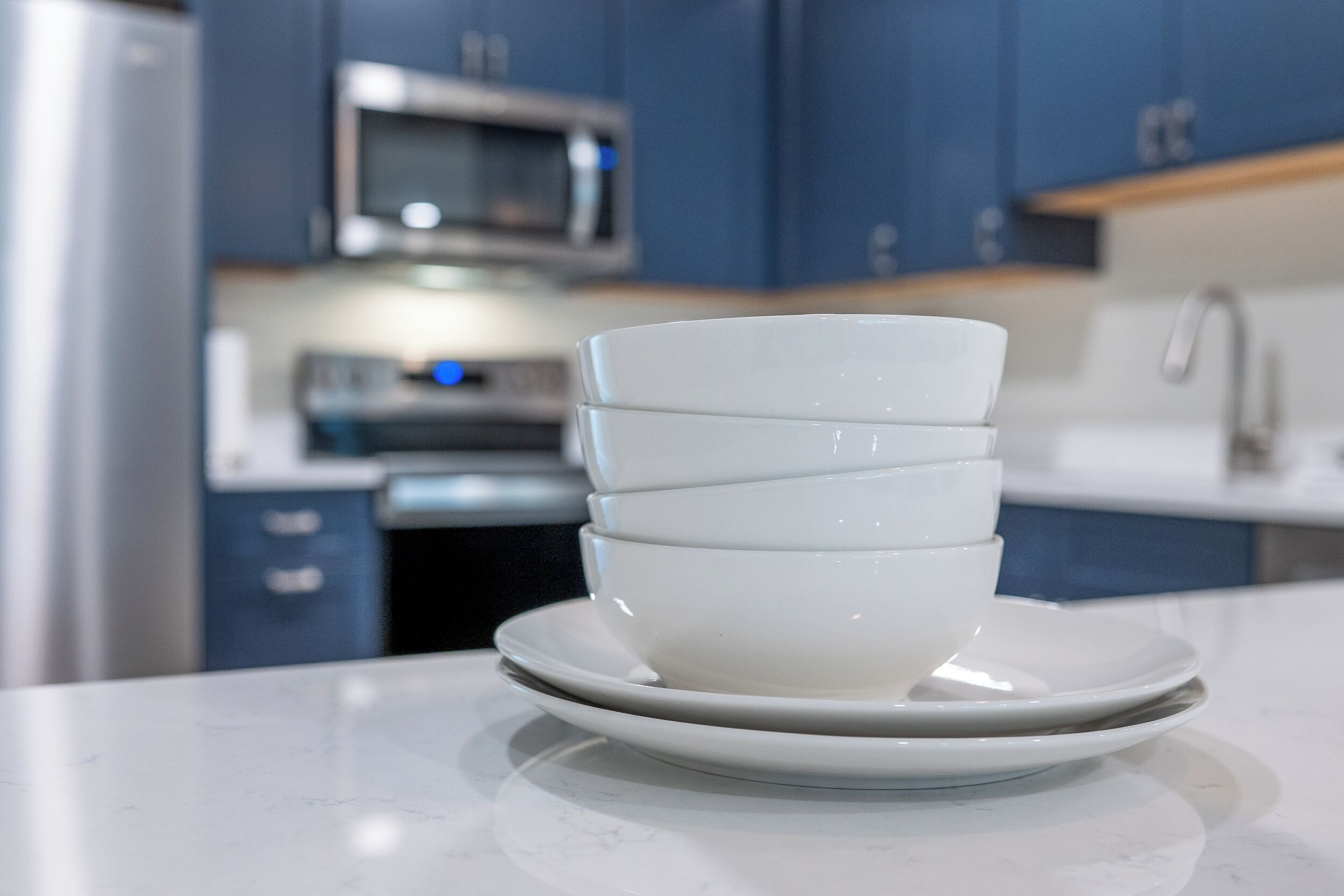 A stack of white bowls on a white plate in a modern kitchen with blue cabinets and stainless steel appliances.
