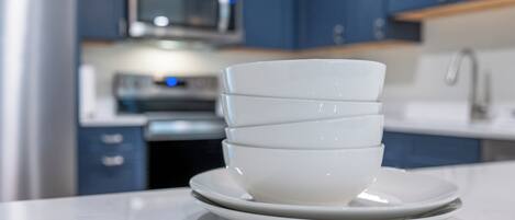 A stack of white bowls on a white plate in a modern kitchen with blue cabinets and stainless steel appliances.