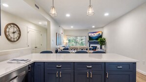 Una cocina moderna con armarios oscuros, encimera de mármol, iluminación colgante y una zona de comedor con vistas.