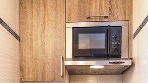 Cocina compacta con armarios de madera, un lavamanos de acero inoxidable y un microondas integrado.