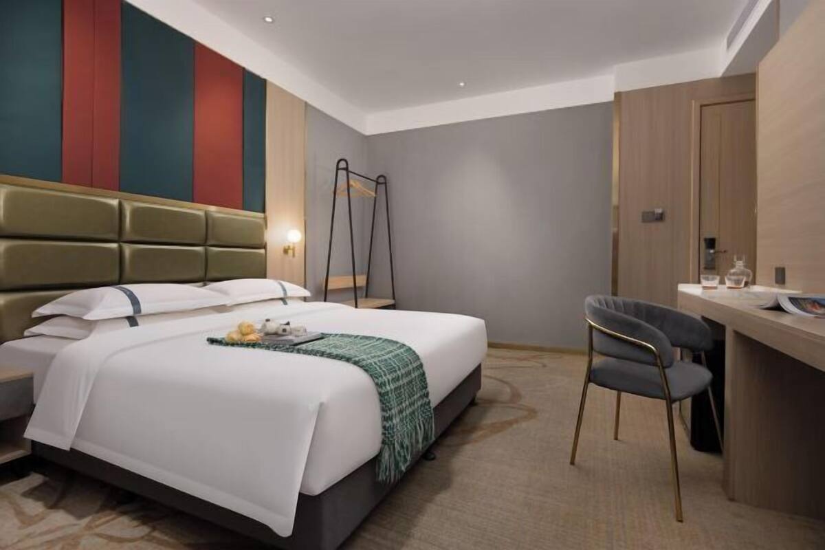 A hotel room with a bed, a desk, a chair, and a mirror.