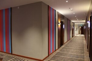 Pasillo de hotel con paredes a rayas, suelo alfombrado y puertas que dan a las habitaciones.