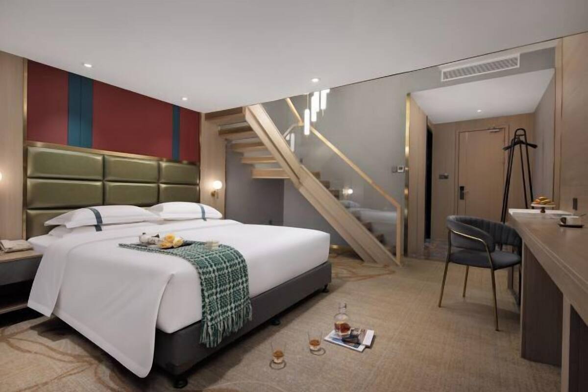 A modern hotel room with a bed, desk, chair, and a staircase.