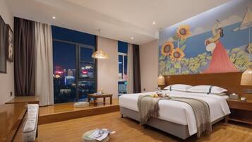 Habitación de hotel con un ventanal grande, una cama, una mesita de noche y un mural en la pared.