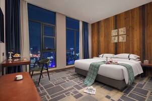 Habitación de hotel con una cama grande, un escritorio, una silla y vistas de la ciudad de noche.