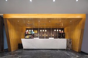 Una zona de recepción con mostrador de mármol, paneles de madera e iluminación colgante.