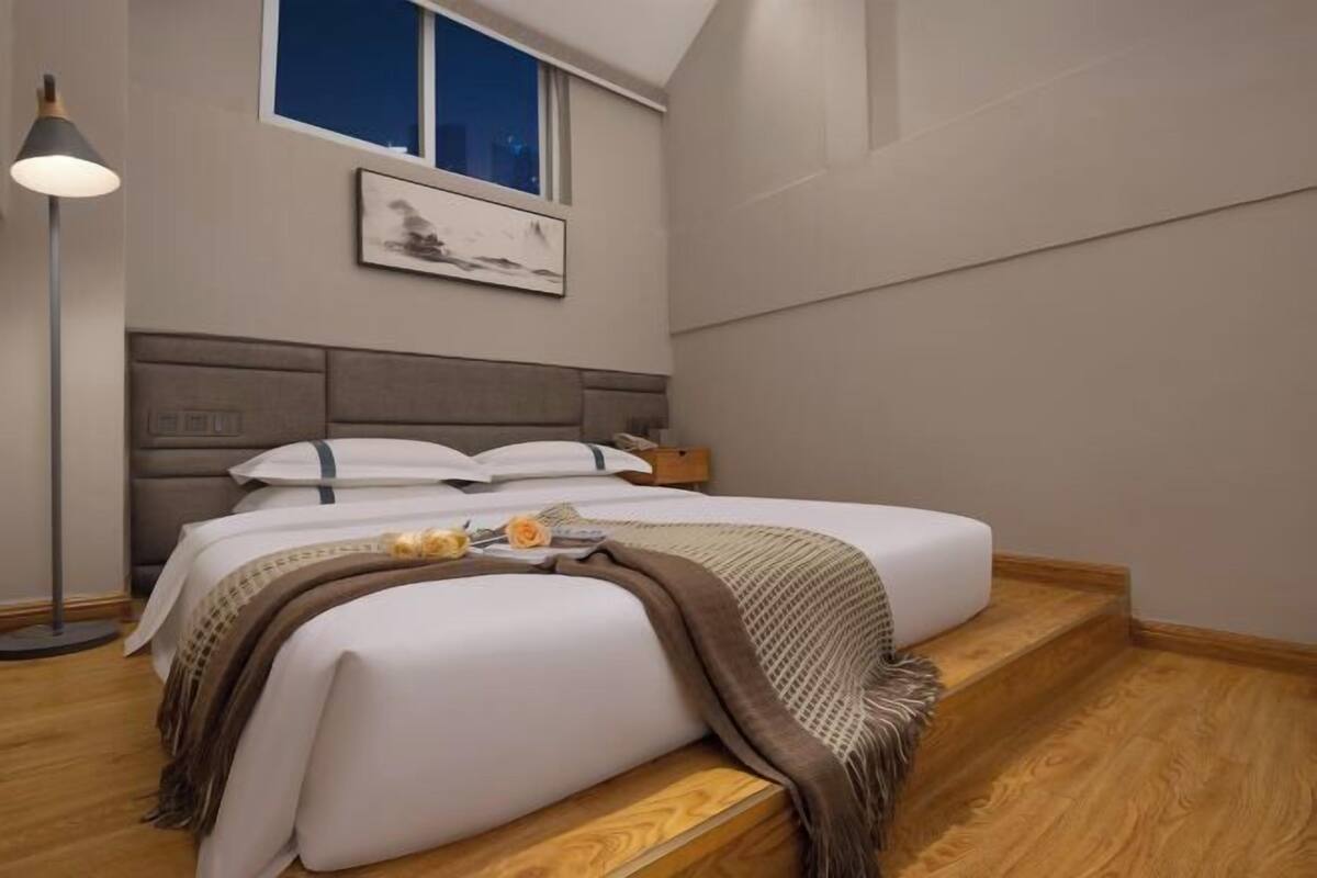 A bedroom with a bed, a nightstand, a lamp, a window, and a painting on the wall.