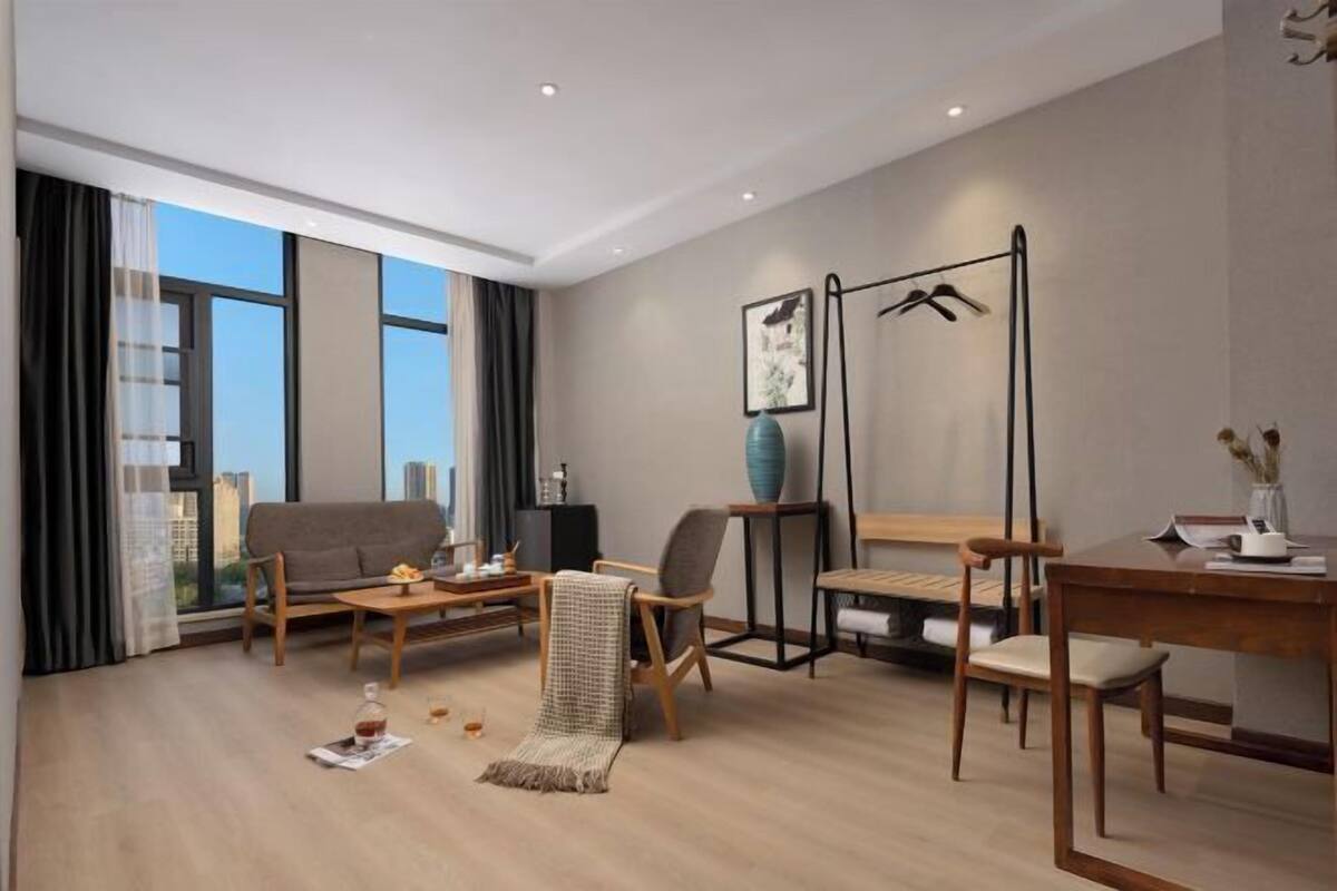 A modern living room with a sofa, coffee table, and chairs, a dining table, a large window with curtains, and a hanging light fixture.