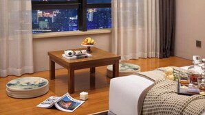 A hotel room with a wooden table, a view of a cityscape at night, a bed with a white cover, and a window with curtains. - Aimeite Boutique Hotel (Changyuan)