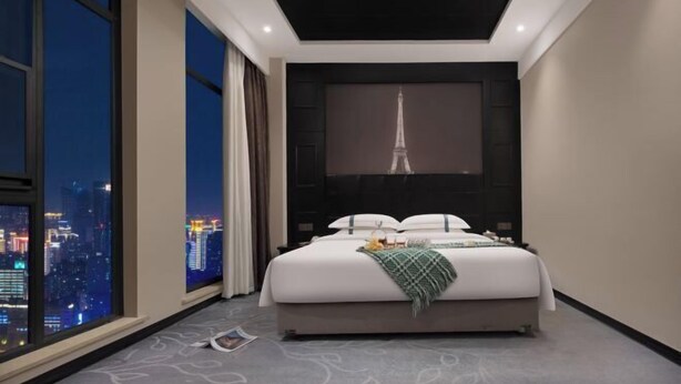 A modern hotel room with a large bed, a city view, and a wall-mounted screen displaying the Eiffel Tower. - Aimeite Boutique Hotel (Changyuan)