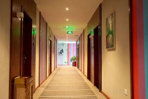 A hotel corridor with doors on both sides, a carpeted floor, and a green exit sign. - Aimeite Boutique Hotel (Changyuan)