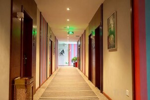 Pasillo de hotel con puertas a ambos lados, piso alfombrado y señal de salida verde.