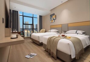 Ein Hotelzimmer mit zwei Betten, einem Schreibtisch mit einer Tasse, einem Stuhl und einem großen Fenster mit Blick auf die Stadt.