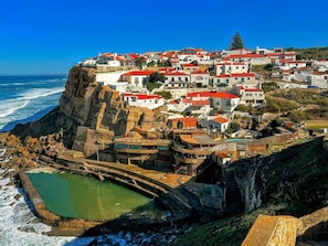 Un pueblo costero con edificios en un acantilado, un muro de contención y una pequeña alberca.