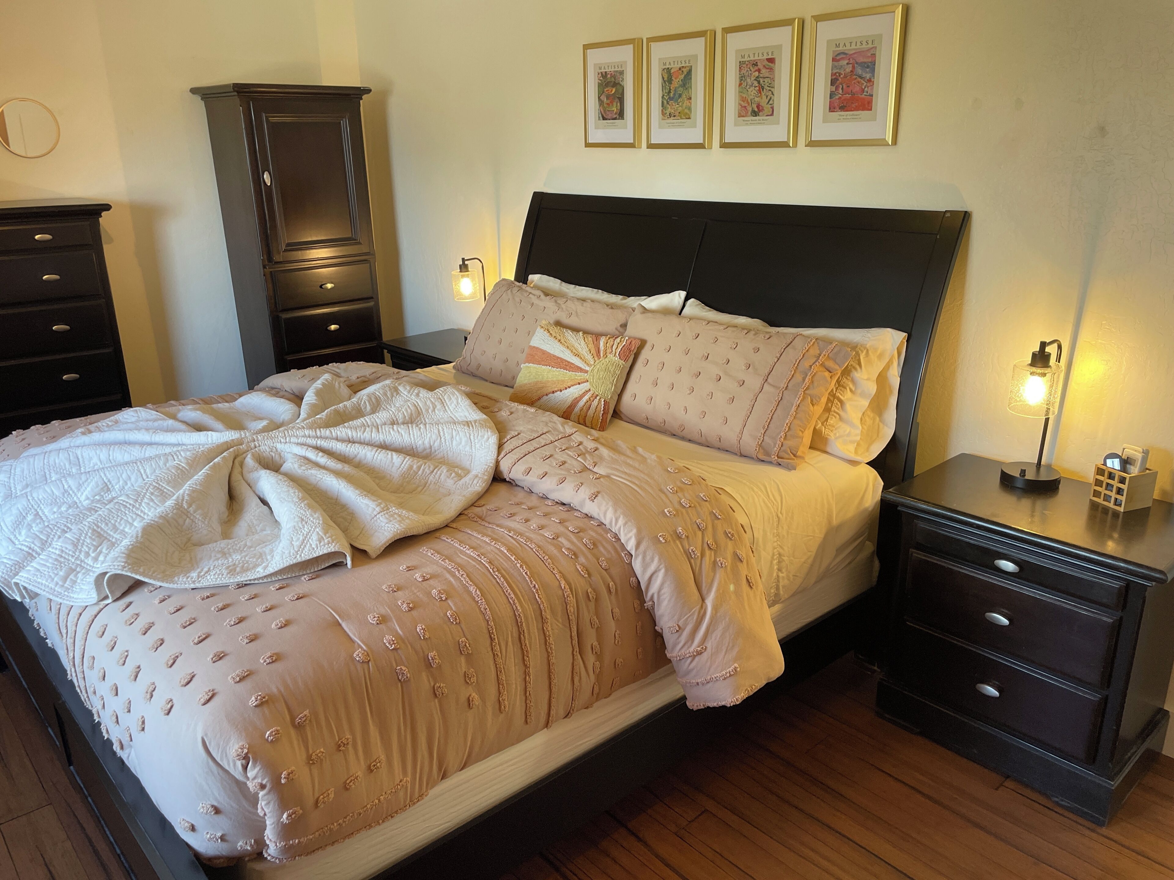 Un lit bien fait, agrémenté d’un grand coussin décoratif, une table de chevet avec une lampe et une commode avec des tiroirs.