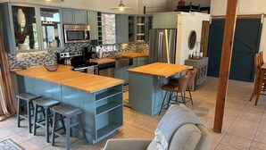 Eine moderne Küche mit Kochinsel, Barhocker und Essbereich mit Sofa und Sesseln.