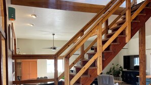 Eine Holztreppe führt zu einer zweiten Etage, ein Küchenbereich mit einer großen Kochinsel und ein Wohnzimmer mit Fernseher und Sitzgelegenheiten.