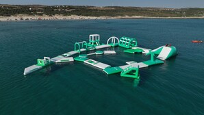 Une plateforme flottante dotée de diverses installations, notamment un toboggan et des espaces de détente, située sur une étendue d’eau.