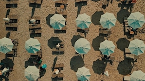 Vue aérienne d’une plage avec plusieurs rangées de transats et de parasols.