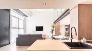 A modern kitchen with a central island, a dining area with a table and chairs, and a living room with a sofa and a TV.