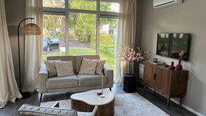 A modern living room with a sofa, coffee table, and a TV mounted on the wall. - Wellness Lodge Hottub on the Salland Ridge in Hellendoorn (Haarle)