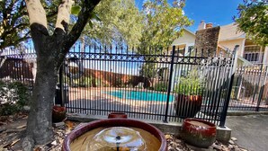 Un espace jardin agrémenté d’une grande fontaine décorative, d’une clôture en métal et d’une piscine en arrière-plan.