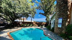 Une piscine dotée d’une terrasse en bois, d’une échelle en métal et d’un mur en briques sur lequel est affiché un panneau indiquant les heures d’ouverture de la piscine.