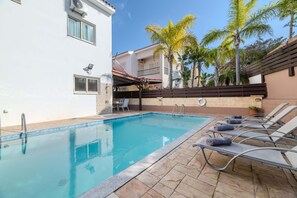 A swimming pool with lounge chairs, a white building with a balcony, and palm trees. - Villa Maria - Charming Pernera Getaway (Protaras)