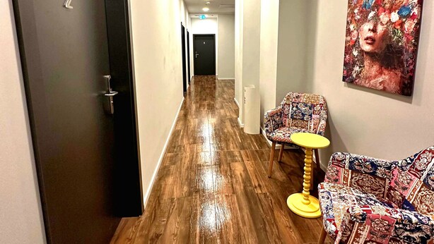 A hallway with wooden flooring, a door labeled '2', a chair with a patterned cushion, and a painting on the wall. - Hotel FFA 62 (Berlin)