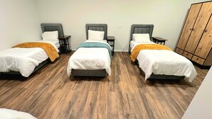 A room with three single beds, each with a wooden headboard, a small bedside table, and a nightstand. The room has a wooden floor and a wardrobe with a wooden finish. - Hotel FFA 62 (Berlin)