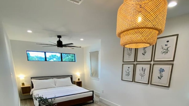 Une chambre moderne avec un lit, un plancher en bois, un ventilateur de plafond et des lampes fixées au mur.
